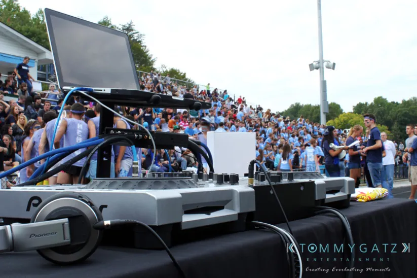 DJ equipment set up on a table at an outdoor event with a large crowd of people in the background.