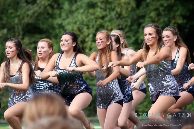 A group of dancers in sparkly outfits performs a synchronized routine outdoors.