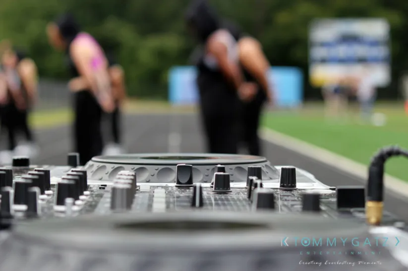Close-up of a DJ mixer with blurred people standing on a track in the background.