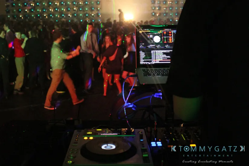 DJ performing at a dance event with a crowd enjoying the music and colorful lights creating a lively atmosphere.