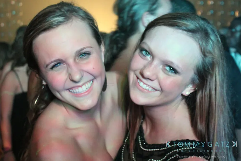 Two people smiling at a party, with others in the background.