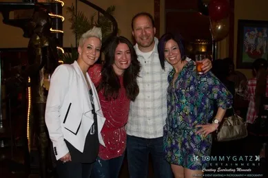 Four people smiling and posing together indoors, with festive decorations in the background.