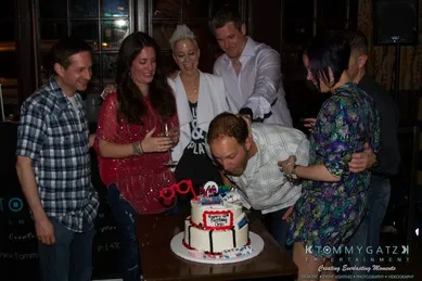 A group of people gathered around a man blowing out candles on a decorated cake at a celebration.