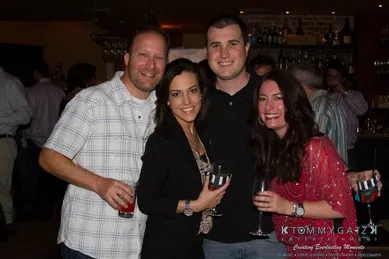 Four people are smiling and posing together at a social event, holding drinks.