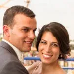 A couple smiling outdoors with blurred amusement park rides in the background.
