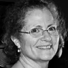 Black and white photo of a person smiling, wearing glasses and earrings, with curly hair.