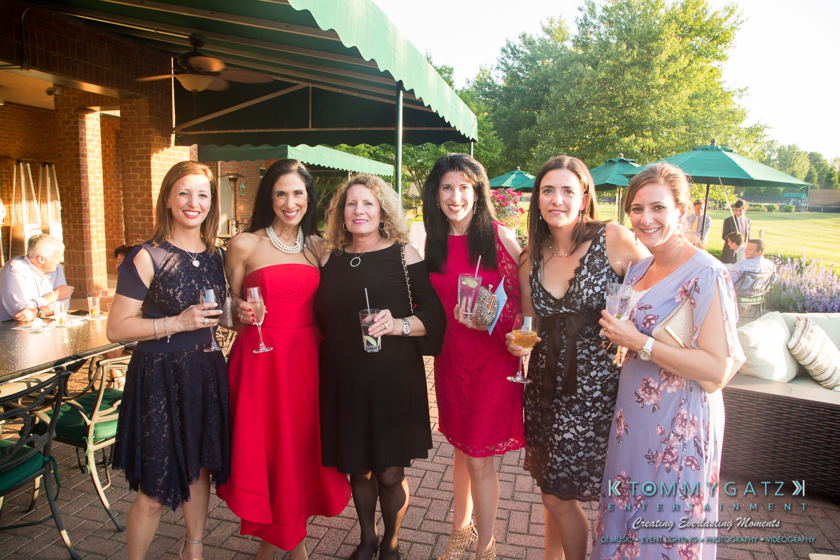 Garbis-Grad-Edits-lowres-Watermark-118 - TOMMY GATZ ENTERTAINMENT Six women in formal attire posing together outdoors, holding drinks, with greenery and a building in the background.