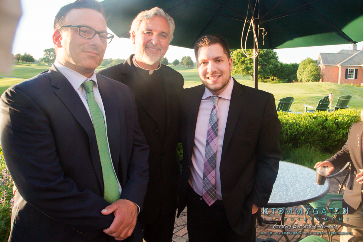 Garbis-Grad-Edits-lowres-Watermark-120 - TOMMY GATZ ENTERTAINMENT Three men in suits and ties are posing outdoors near a table. A brick building and lawn are visible in the background.
