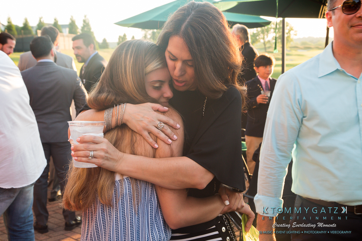 Garbis-Grad-Edits-lowres-Watermark-126 - TOMMY GATZ ENTERTAINMENT Two women embracing at an outdoor event. One holds a drink, and they are surrounded by other attendees.