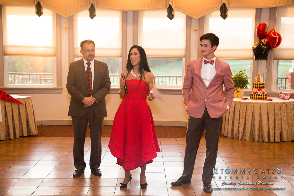 Garbis-Grad-Edits-lowres-Watermark-140 - TOMMY GATZ ENTERTAINMENT Three people in formal attire are standing indoors. The woman in the center holds a microphone and appears to be speaking.