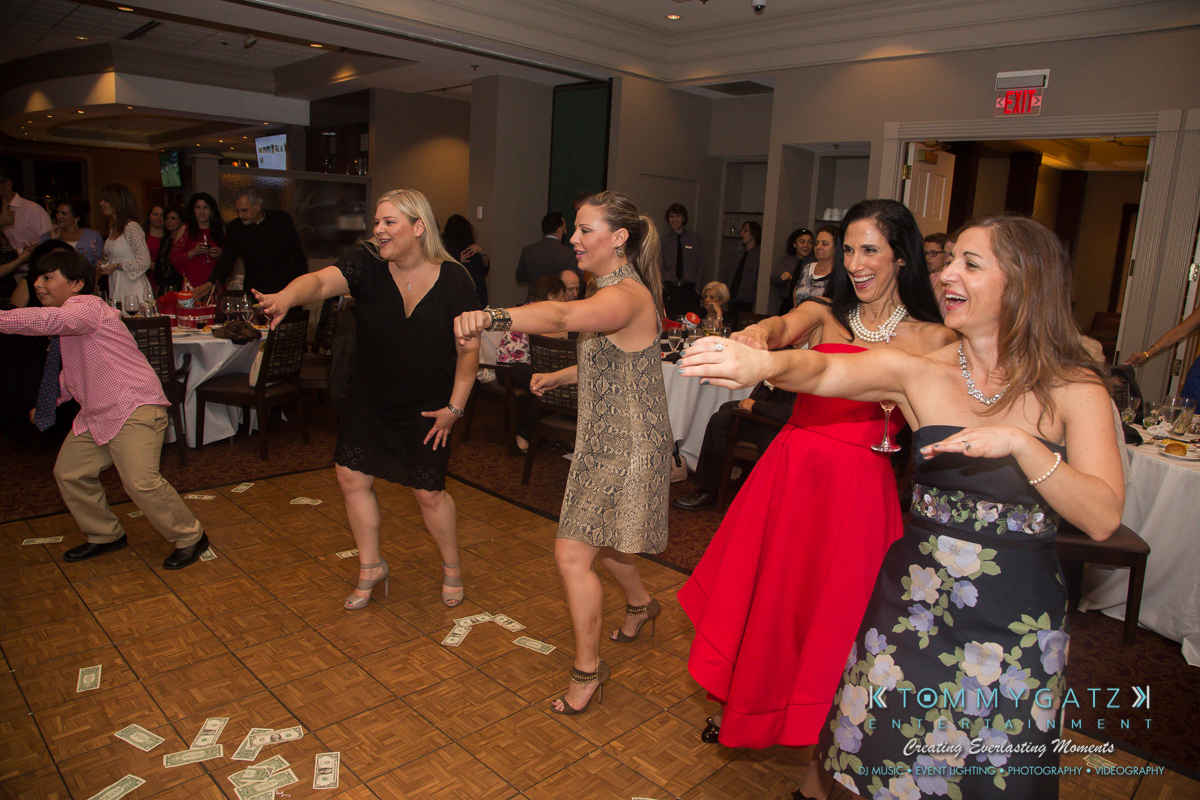 Garbis-Grad-Edits-lowres-Watermark-340 - TOMMY GATZ ENTERTAINMENT A group of people dancing on a wooden floor with scattered dollar bills. Tables and more people are in the background.