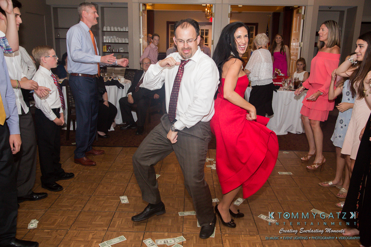 Garbis-Grad-Edits-lowres-Watermark-359 - TOMMY GATZ ENTERTAINMENT Two people dance enthusiastically on a wooden floor surrounded by a small crowd seated at tables. Dollar bills are scattered on the floor.