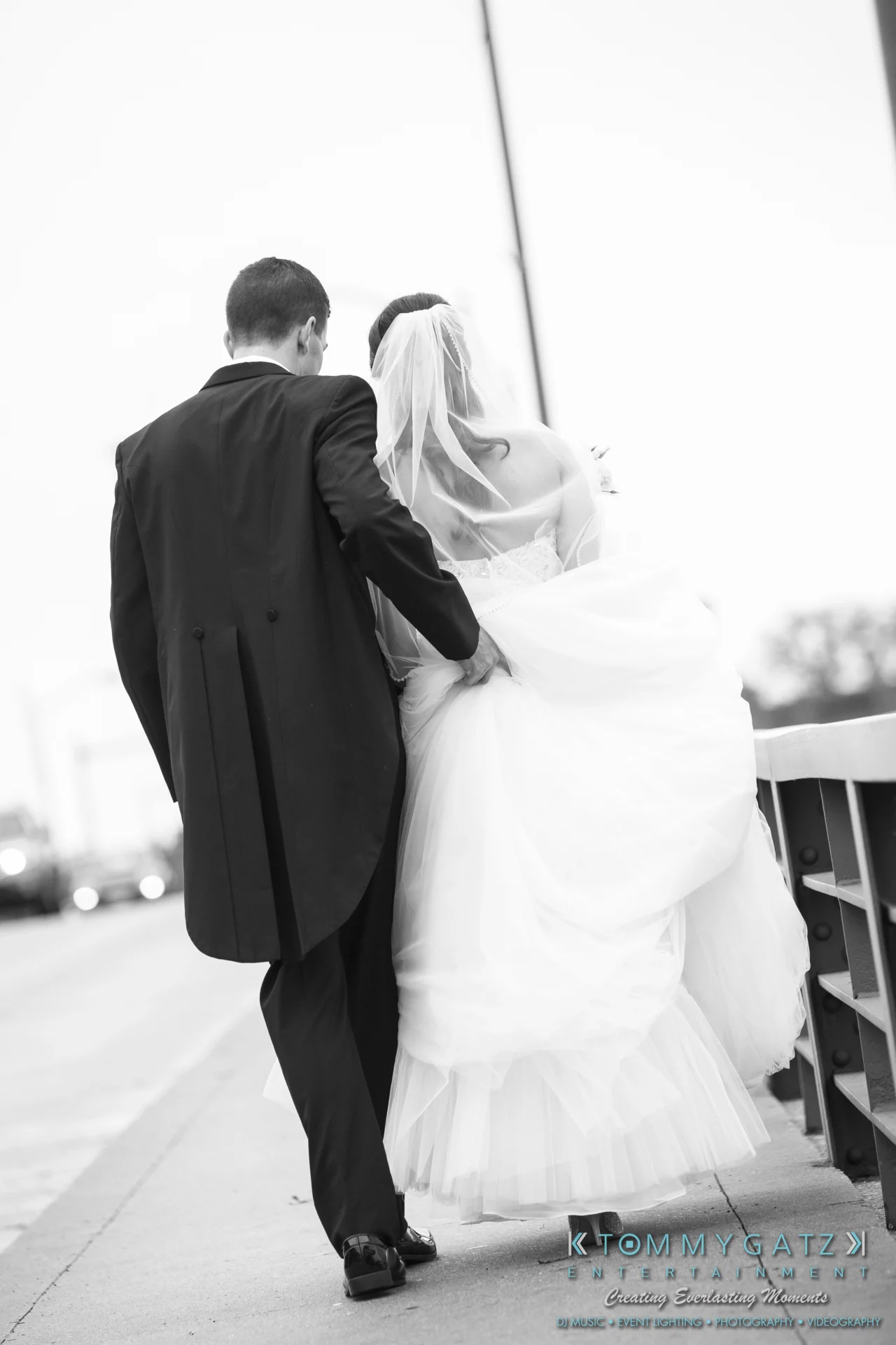 Bride and groom walking together on a road, with the bride holding her gown and the groom supporting her.