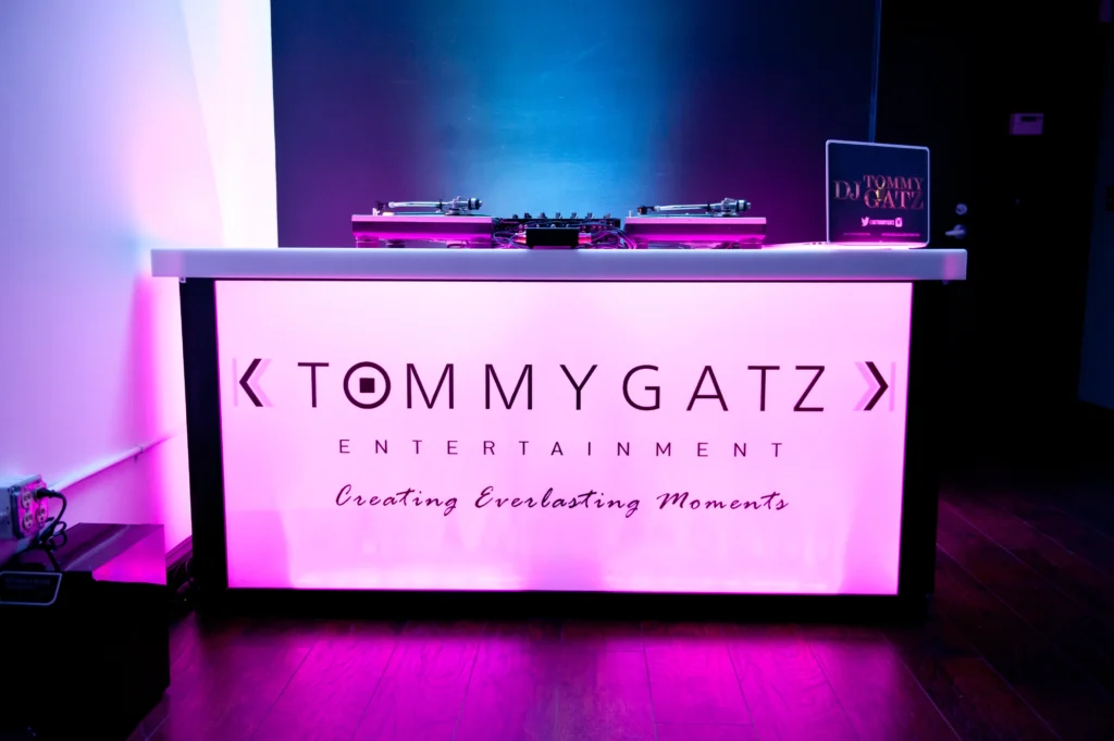 A DJ booth labeled "Tommy Gatz Entertainment" with turntables and a mixer on top, surrounded by purple and blue lighting.