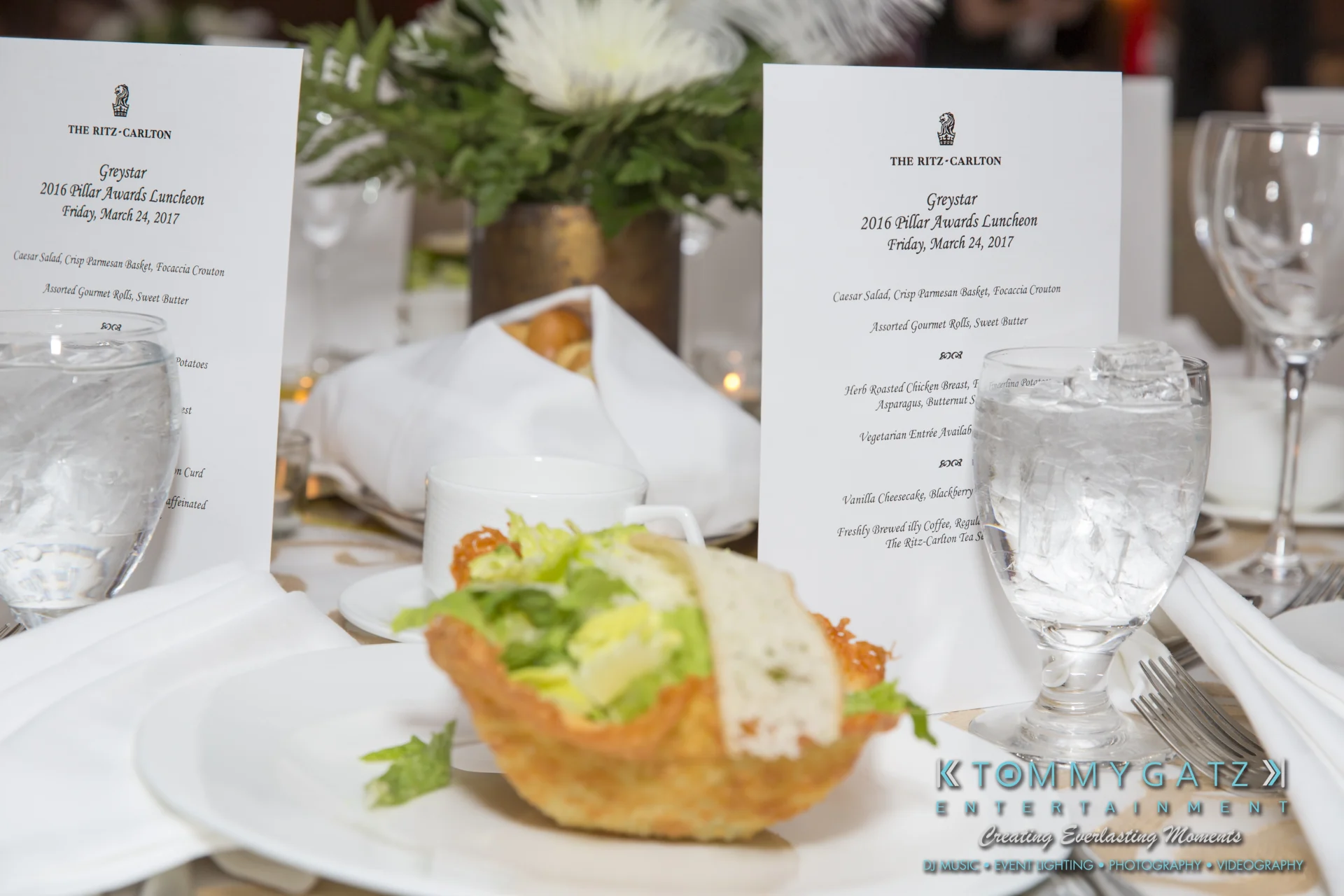 Close-up of a formal dining table setting with a Caesar salad in a bread bowl, water glasses, and event menus at The Ritz-Carlton.