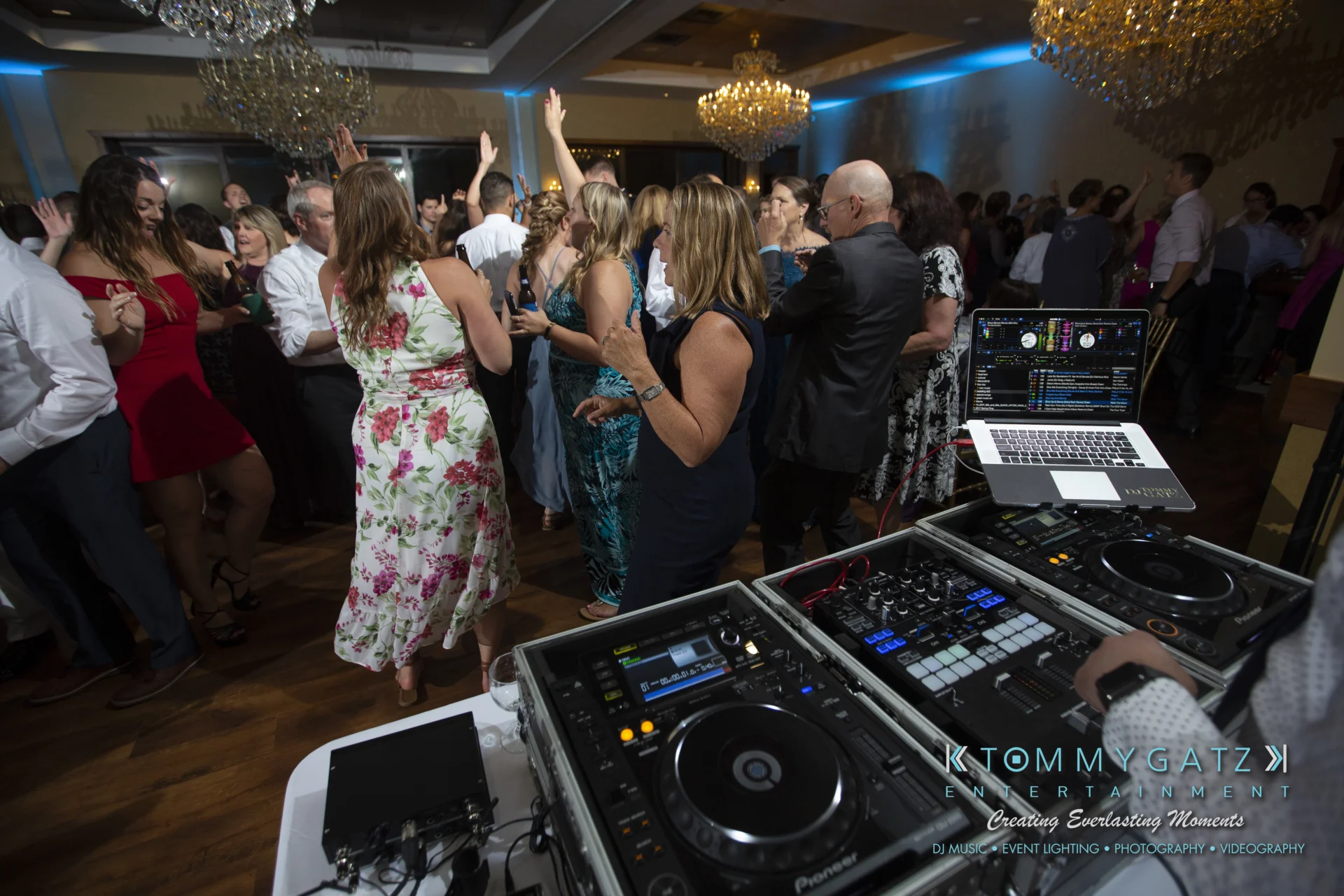 A group of people dancing in a ballroom with a DJ booth in the foreground.