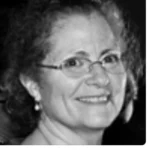 Black and white photo of a person with glasses and short curly hair, smiling slightly.