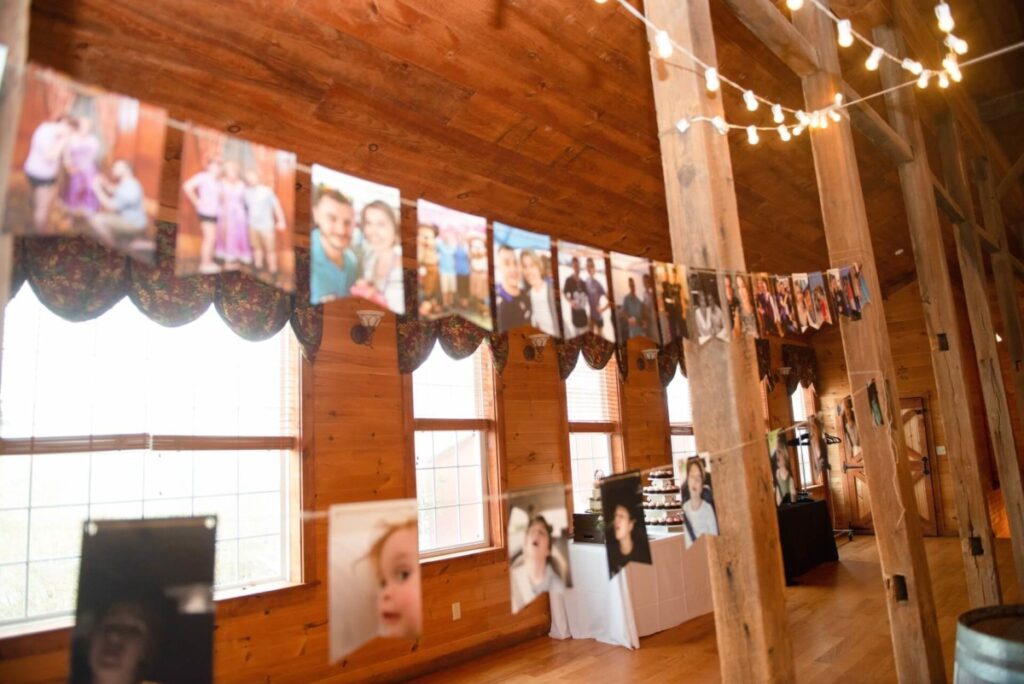 Christine-Jon-Wedding-Blog-54 - TOMMY GATZ ENTERTAINMENT Photos hanging on string in a wooden room with large windows and string lights. Tables and curtains are in the background.