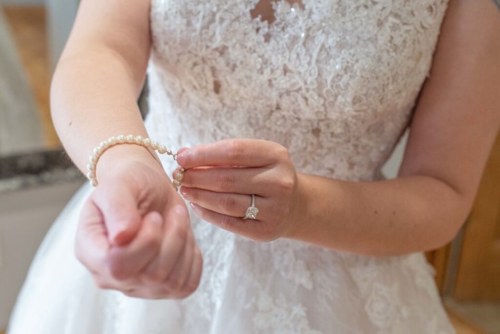 Christine-Jon-Wedding-Blog-7 - TOMMY GATZ ENTERTAINMENT A bride in a lace wedding dress puts on a pearl bracelet.