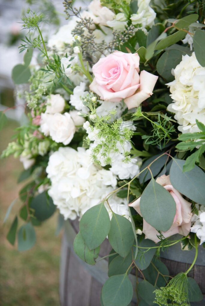 Christine-Jon-Wedding-Blog-71 - TOMMY GATZ ENTERTAINMENT A bouquet with pink roses, white hydrangeas, and green foliage, arranged in a wooden barrel.