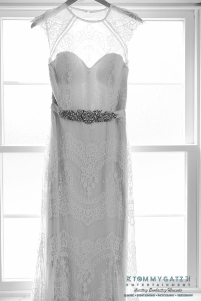 Jennifer-Rudi-Highlights-Low-res-74 - TOMMY GATZ ENTERTAINMENT White lace wedding dress with intricate patterns and a jeweled belt, displayed in front of a bright window.