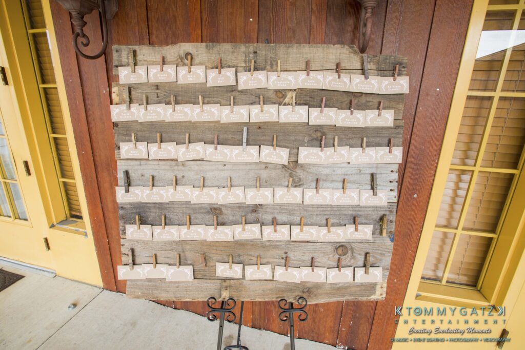 Jennifer-Rudi-Highlights-Low-res-85 - TOMMY GATZ ENTERTAINMENT A wooden seating chart display with rows of beige place cards attached by small clothespins.