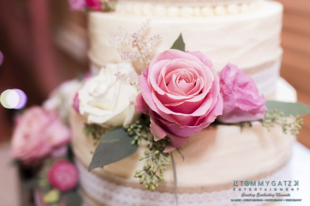 Jennifer-Rudi-Highlights-Low-res-91 - TOMMY GATZ ENTERTAINMENT Close-up of a tiered wedding cake decorated with pink and white roses and greenery.