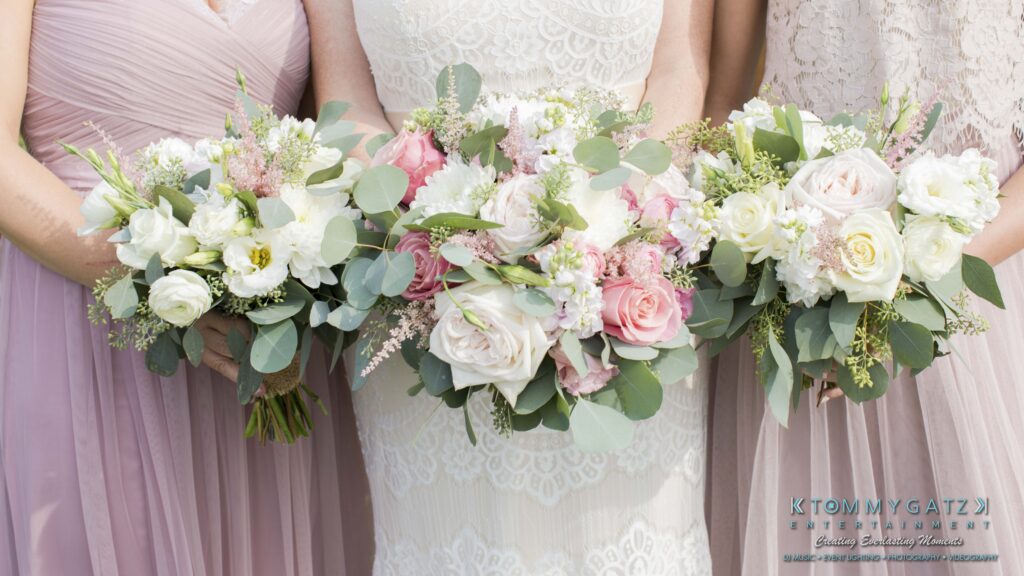 JenniferRudiWeddingFormalPhotos-197 - TOMMY GATZ ENTERTAINMENT Three women in dresses holding bouquets of white and pink roses with greenery.