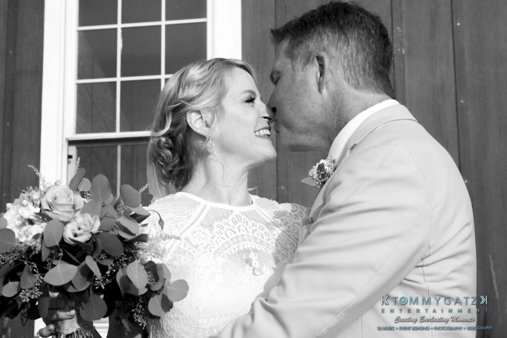 JenniferRudiWeddingFormalPhotos-219 - TOMMY GATZ ENTERTAINMENT A couple smiles at each other holding a bouquet, standing close in front of a windowed door.