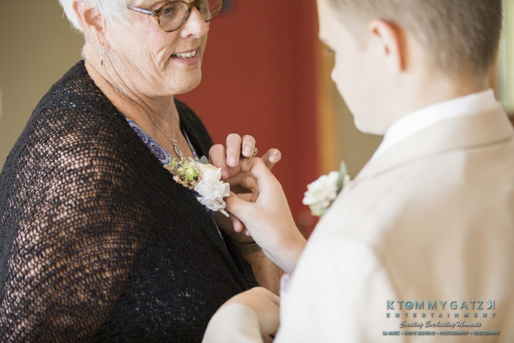 JenniferRudiWeddingPrepPhotos-51 - TOMMY GATZ ENTERTAINMENT An elderly woman smiles as a young boy in a suit pins a boutonniere to her black shawl.