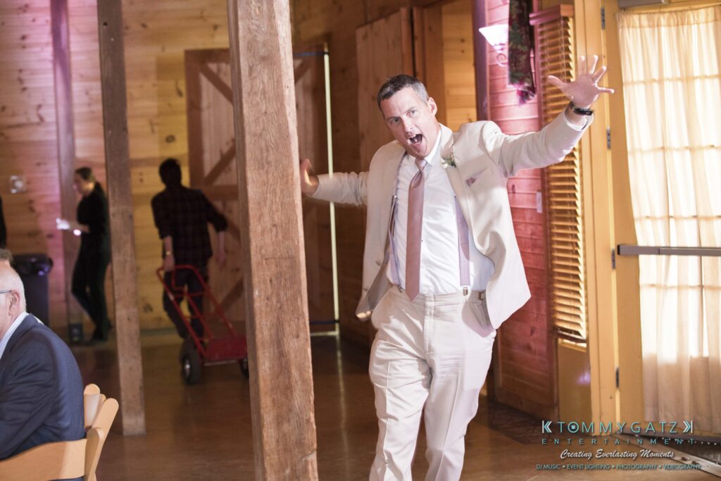 JenniferRudiWeddingReceptionPhotos-292 - TOMMY GATZ ENTERTAINMENT Man in a light suit enthusiastically enters a wooden hall with arms wide open.
