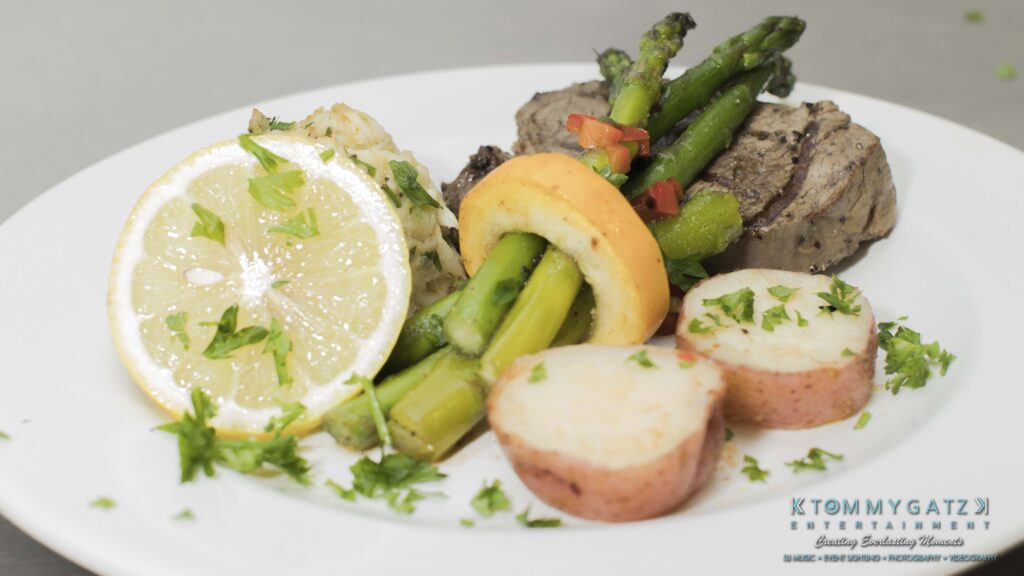 JenniferRudiWeddingReceptionPhotos-312 - TOMMY GATZ ENTERTAINMENT A plate with grilled beef, asparagus, sliced lemon, roasted potato slices, and garnished with herbs.