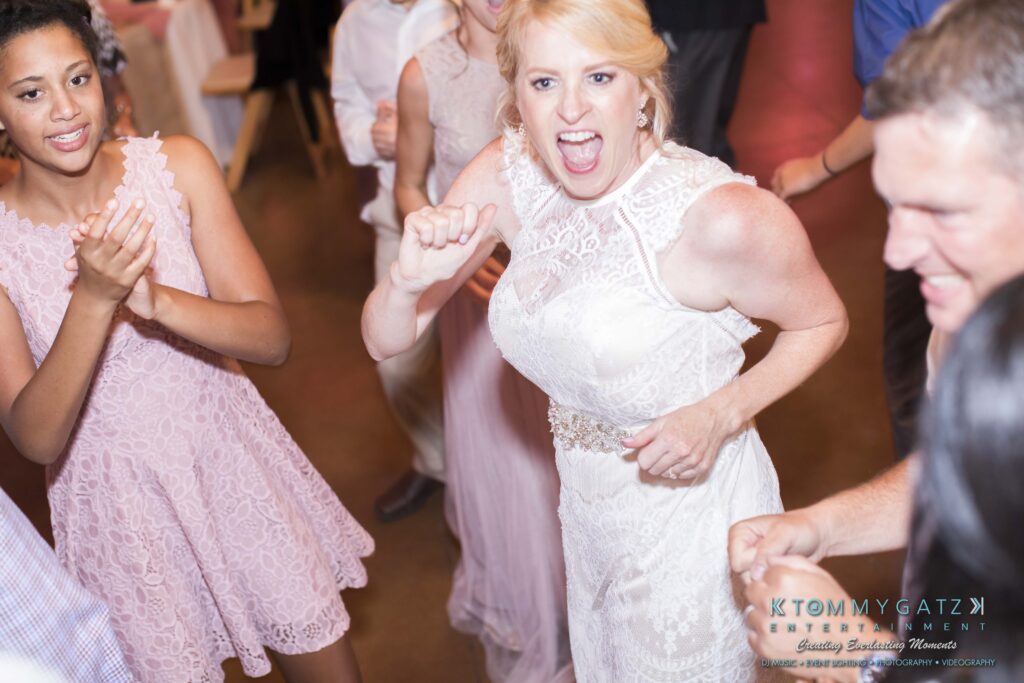 JenniferRudiWeddingReceptionPhotos-368 - TOMMY GATZ ENTERTAINMENT Bride dancing energetically with guests at a wedding reception.