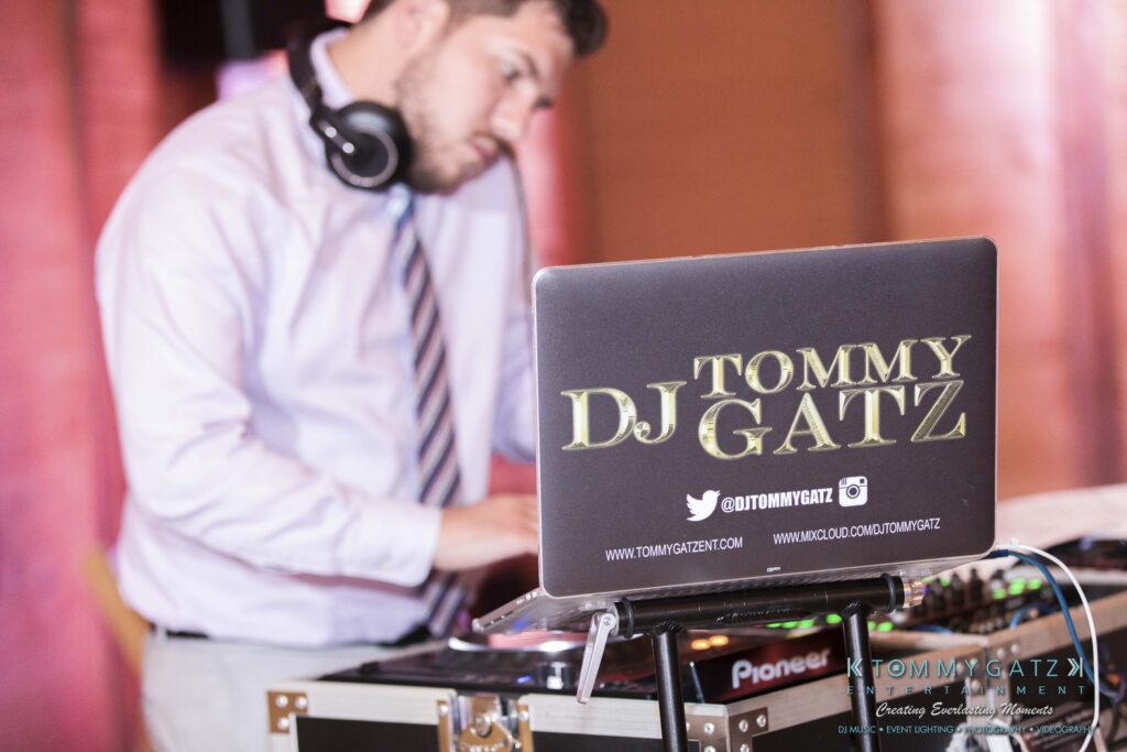 JenniferRudiWeddingReceptionPhotos-373 - TOMMY GATZ ENTERTAINMENT A DJ wearing headphones is mixing music on a laptop and DJ controller. The laptop displays the name "Tommy DJ Gatz" alongside social media information.