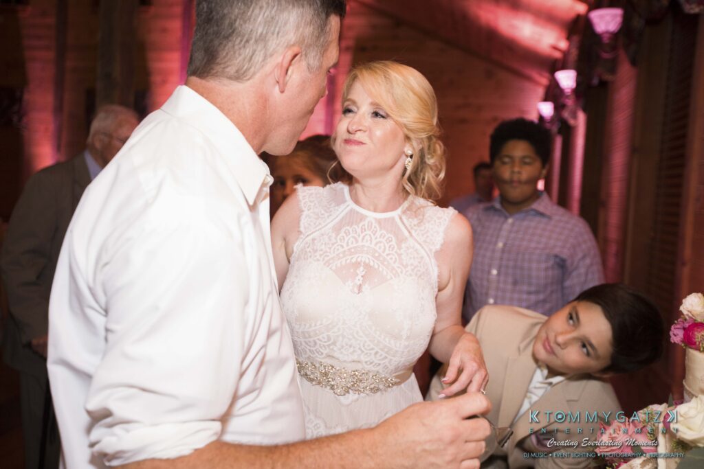 JenniferRudiWeddingReceptionPhotos-389 - TOMMY GATZ ENTERTAINMENT A woman in a white dress interacts with a man in a white shirt at an indoor event. Two others look on in the background.