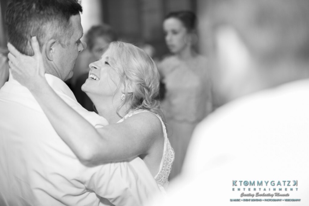 JenniferRudiWeddingReceptionPhotos-393 - TOMMY GATZ ENTERTAINMENT A couple shares a joyful embrace while dancing at an event, surrounded by other attendees.
