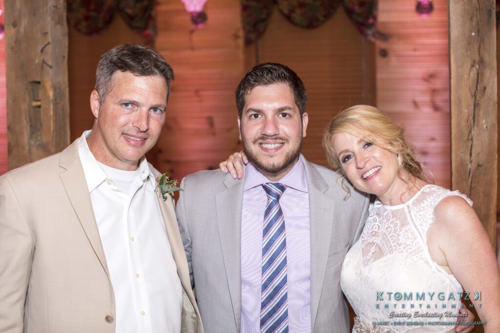 JenniferRudiWeddingReceptionPhotos-396 - TOMMY GATZ ENTERTAINMENT Three people dressed formally, two men and a woman, smiling and posing together indoors.
