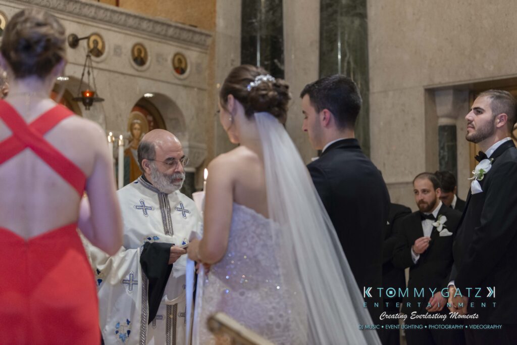 A wedding ceremony with a bride and groom facing an officiant in a church. A bridesmaid in red is in the foreground, and guests watch from the pews.