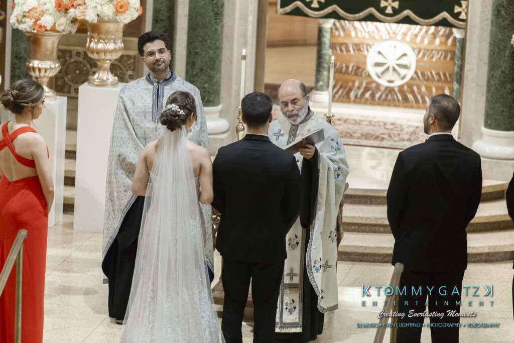 A wedding ceremony in a church with a bride, groom, two priests, and two attendants, one in a red dress.