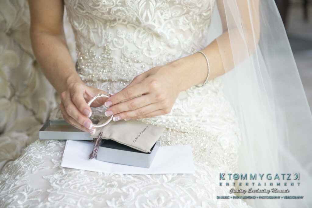 Urania-Aristidis-060218-PREP-Low-Res-WM-117 - TOMMY GATZ ENTERTAINMENT Bride in an ornate gown holding a bracelet, sitting on a chair with a silver box and card on her lap.