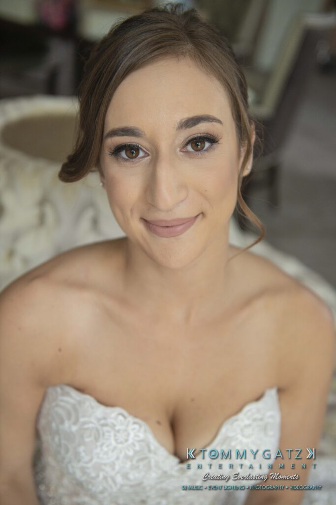 A woman in a white strapless dress looks into the camera with a slight smile, posing indoors.