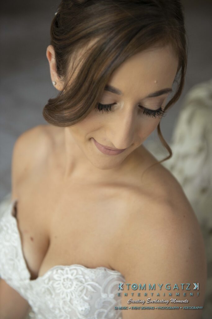 A bride in a white strapless gown looks down with a gentle smile, showing a side-swept hairstyle.