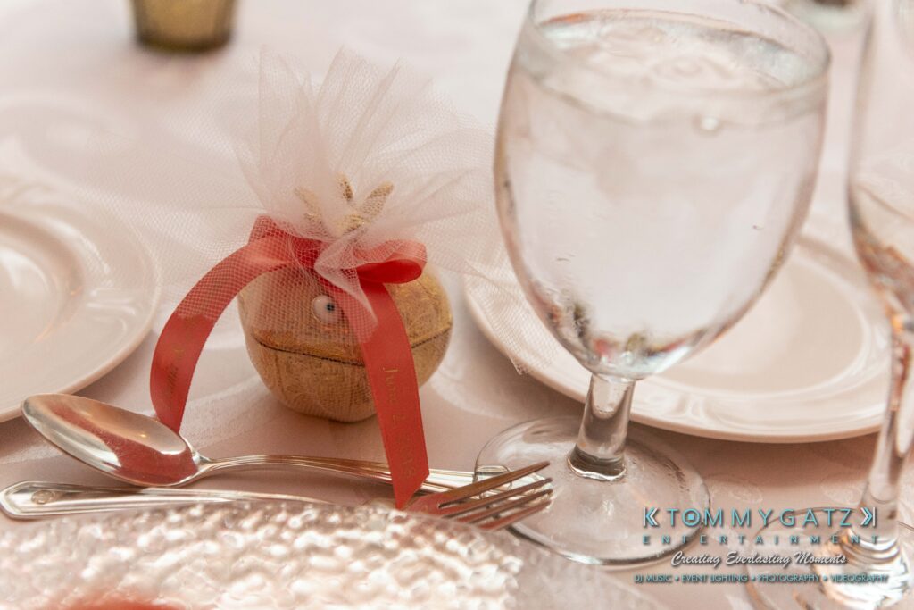 Table setting with a glass of water, a small wrapped gift with a red ribbon, and a place setting. Plates, a knife, and a fork are arranged on a white tablecloth.