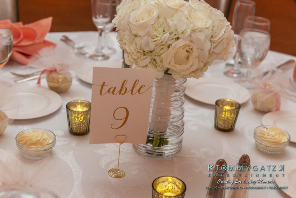Table with a floral centerpiece, labeled "table 9," surrounded by votive candles and small dessert cups, set for an event.