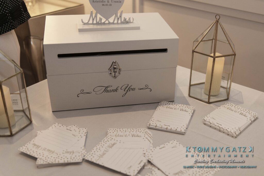 White thank you card box with a lock on a table, surrounded by gold lanterns and wedding advice cards, set up for guests to write notes.