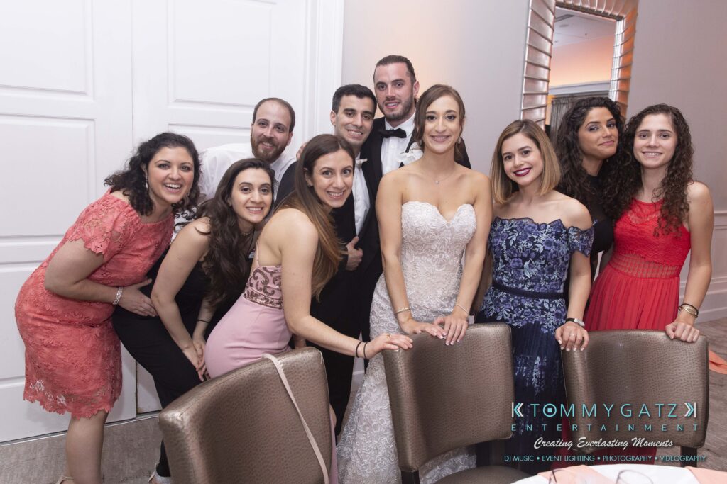 A group of people posing together indoors, with one woman in a white dress in the center.