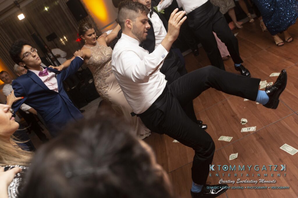 People dancing energetically on a wooden dance floor at a party, with some cash scattered on the floor.