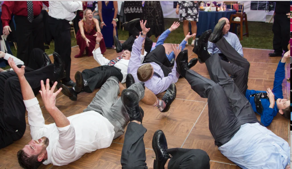 People in formal attire lying on a dance floor, raising their arms and legs, engaged in a choreographed or playful activity.