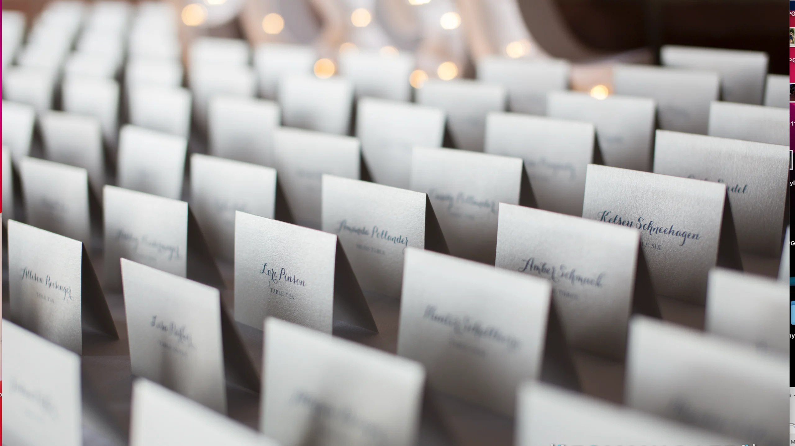 A neatly arranged set of white place cards displays names in elegant script at an event, with soft lights in the background.