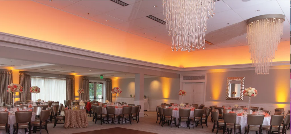 2Event-Lighting-_-Decor-Photo-_2-Weddings- - TOMMY GATZ ENTERTAINMENT An elegant banquet hall with round tables set for an event. The room features soft lighting, floral centerpieces, mirrors, and large crystal chandeliers hanging from the ceiling.